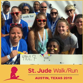 A group of people smile against a St. Jude step and repeat featuring the St. Jude logo.