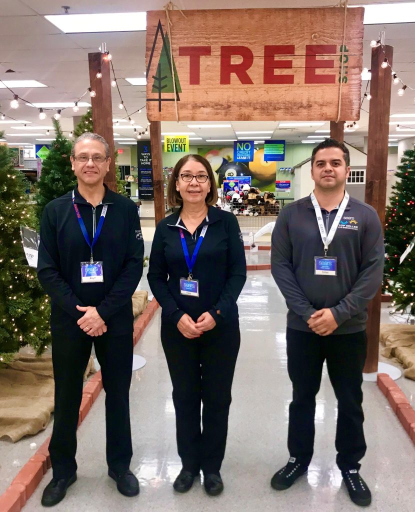 Sears associates stand in front of merchandise at a Sears store.