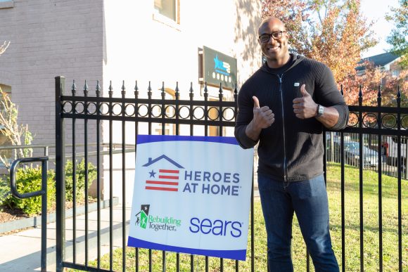 DeMarcus Ware gives two thumbs up in front of a project sign for Rebuilding Together and Heroes at Home completed in partnership with Sears.